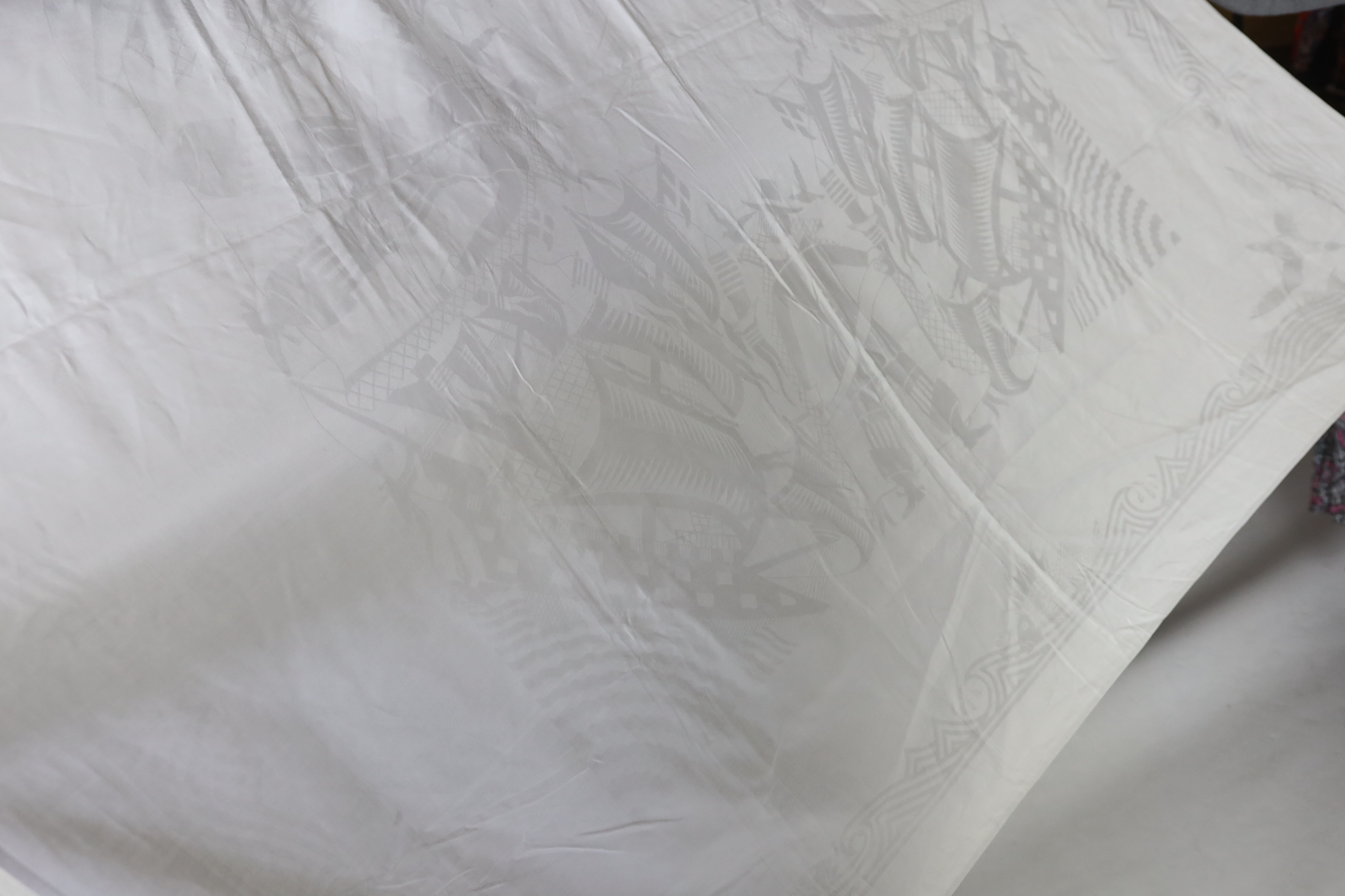 An early 20th century white linen damask table cloth, the design partly inspired by William de Morgan with galleons and fin backed fish in swirling water and tall figures with scrolls, possibly a reference to the Pilgrim